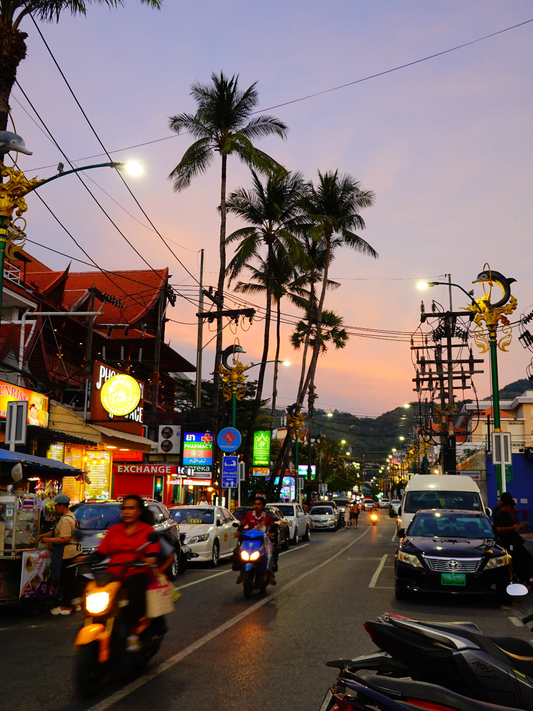 Street scene with palm trees, streetlights, and colorful buildings at dusk.